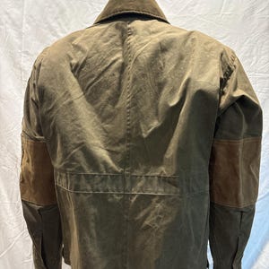 Puede incluir: Una chaqueta de lona marr&oacute;n con parches de cuero marr&oacute;n en los codos. La chaqueta tiene un cuello abotonado y una cremallera.