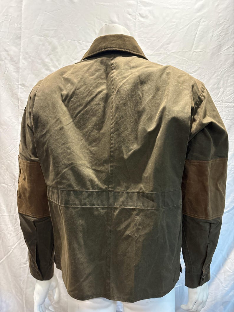 Puede incluir: Una chaqueta de lona marr&oacute;n con parches de cuero marr&oacute;n en los codos. La chaqueta tiene un cuello abotonado y una cremallera.