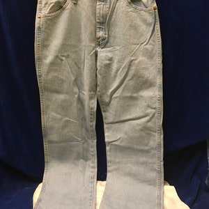 May include: Light blue denim jeans with a straight leg and a slight flare at the bottom. The jeans have a button fly and five pockets.