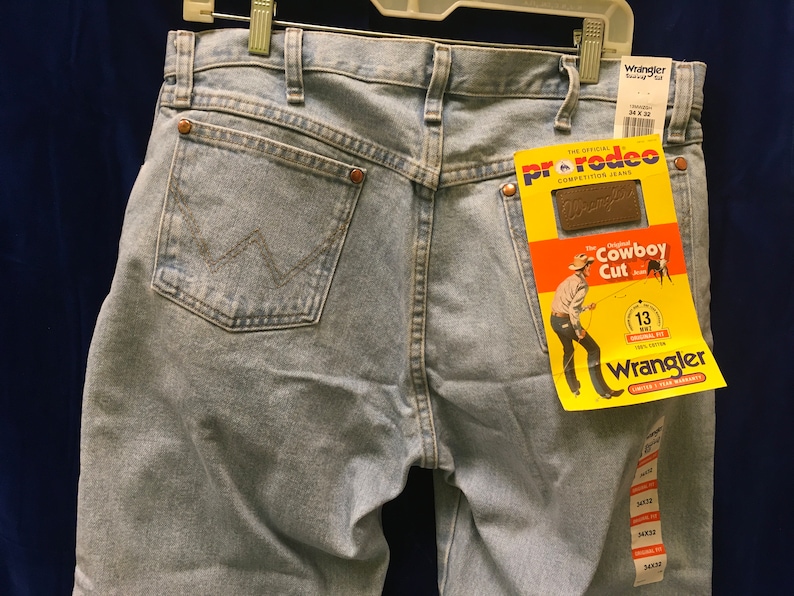 May include: Light blue denim jeans with a brown leather Wrangler label and a yellow tag that reads "The Original Cowboy Cut" with a Wrangler logo.