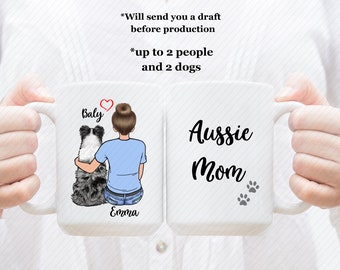 May include: White ceramic mug with a design of a woman with a bun in her hair sitting with a dog. The text "Baly" and "Emma" are on the mug. The other side of the mug has the text "Aussie Mom" with paw prints.