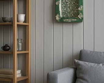 Può includere: Una nicchia da parete ad arco di colore verde con un motivo floreale bianco sul pannello posteriore interno e quattro piccoli accenti bianchi a forma di diamante sulla cornice esterna, montata su una parete a pannelli verticali sopra un divano grigio.