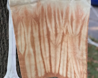 May include: A white tote bag with a tie-dye pattern in shades of brown and orange. The bag has a natural fabric texture.
