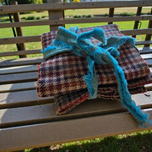 May include: A bundle of patterned fabric squares in brown, burgundy, and cream, secured with a turquoise ribbon. The fabric features a houndstooth pattern. The bundle is on a wooden bench in an outdoor setting.