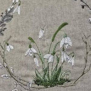 May include: Embroidered design of a wreath of white snowdrops with green leaves on a beige linen fabric.