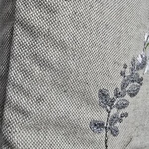 May include: A gray linen pillow with embroidered white flowers and green leaves.