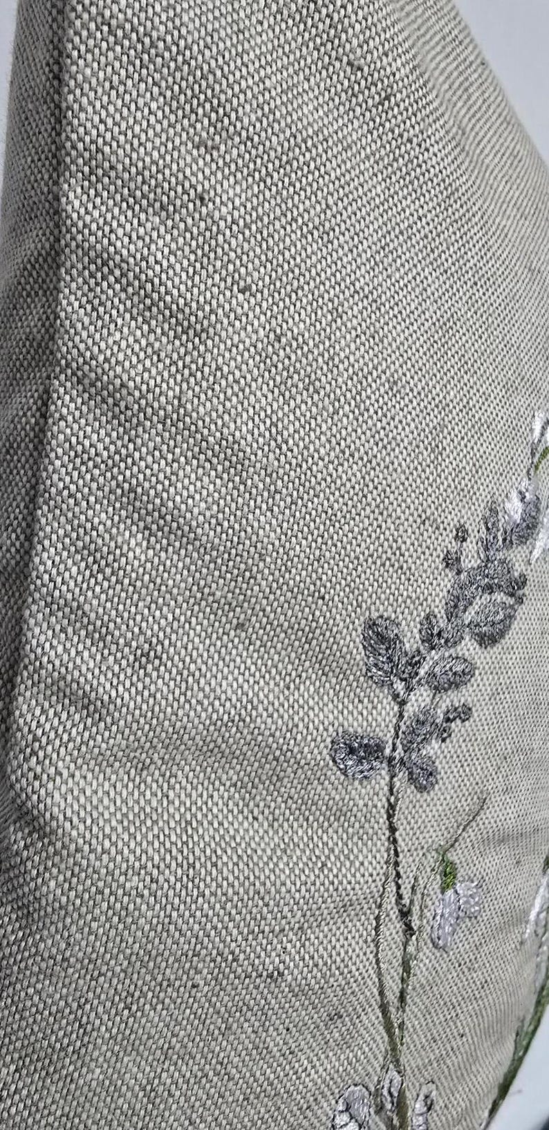 May include: A gray linen pillow with embroidered white flowers and green leaves.