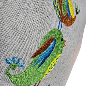 May include: Embroidered birds on a light gray fabric background. The birds are green, blue, yellow, and brown. The birds are perched on a branch with green leaves.