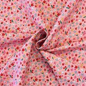 May include: Pink fabric featuring a repeating floral pattern. The design includes tiny red, white, yellow, and blue flowers. The fabric has a soft texture and a slightly creased appearance.