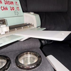 May include: A mint green and white craft cutting machine with a white tray sits on a grey sofa. The machine has a silver roller and a control panel. The text "I CAN DREAM IT, CAN DO IT" is visible. Two silver cup holders are in the foreground.