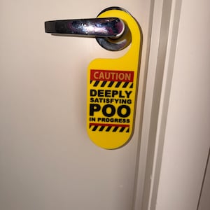 May include: A yellow door hanger with the text "CAUTION DEEPLY SATISFYING POO IN PROGRESS" in black and red. The hanger is hanging on a white door with a chrome handle.