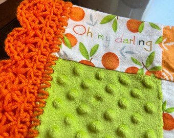 May include: A handmade baby blanket with a vibrant orange crocheted border and a soft, textured lime green fabric. The blanket includes a white fabric section with orange fruit and the words "Oh my darling".