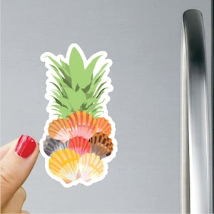 Puede incluir: Un imán con forma de piña con un grupo de conchas de colores en tonos naranja, rosa, rojo y marrón.