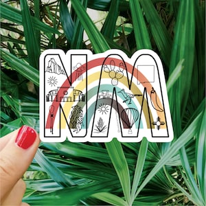May include: A white sticker with a rainbow arch and the letters "NM" in black outline. The letters are filled with various icons representing New Mexico, including a hot air balloon, a chili pepper, a sun, a roadrunner, and a Zia symbol.