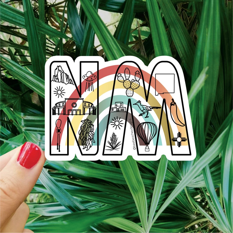 May include: A white sticker with a rainbow arch and the letters "NM" in black outline. The letters are filled with various icons representing New Mexico, including a hot air balloon, a chili pepper, a sun, a roadrunner, and a Zia symbol.