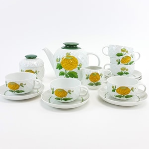 Op de afbeelding: Een wit porseleinen theeservies met een geel bloemenmotief. De set bevat een theepot, een roomkan, een suikerpot en vier kopjes en schoteltjes.