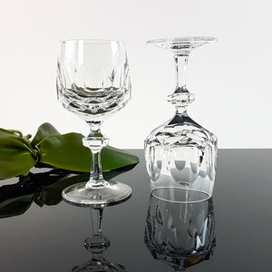 May include: Two clear crystal wine glasses featuring a faceted geometric bowl design and a multi-tiered stem. One glass stands upright while the other is inverted, showcasing the intricate cut patterns on the base and the bowl of the glassware.