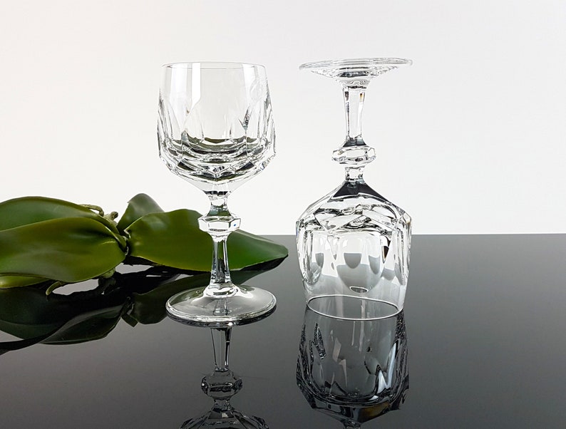 May include: Two clear crystal wine glasses featuring a faceted geometric bowl design and a multi-tiered stem. One glass stands upright while the other is inverted, showcasing the intricate cut patterns on the base and the bowl of the glassware.