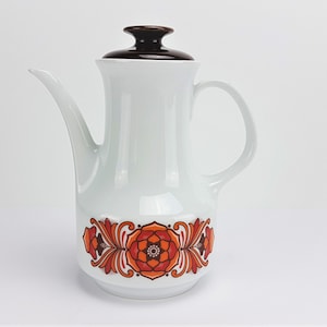 May include: White ceramic coffee pot with a brown lid and orange and brown floral design.