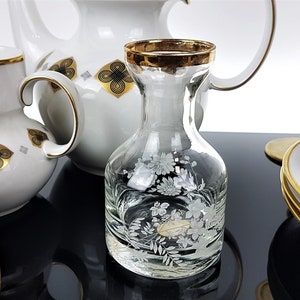 May include: A collection of white porcelain tableware with gold trim and decorative floral and geometric patterns. Includes a pitcher, creamer, plates, and a clear glass carafe with etched floral designs.
