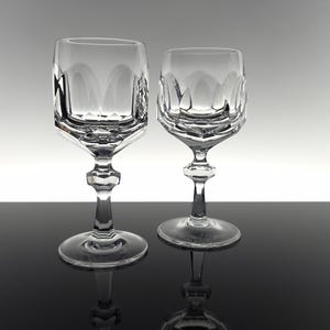 May include: Two clear crystal wine glasses featuring a faceted, geometric bowl design with vertical cut patterns. Each glass has a multi-faceted stem and a circular base, showcasing a reflective, transparent finish with sharp, angular edges.