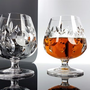 May include: Two clear crystal brandy snifters with a cut glass design. One snifter is empty and the other is filled with amber colored liquid.