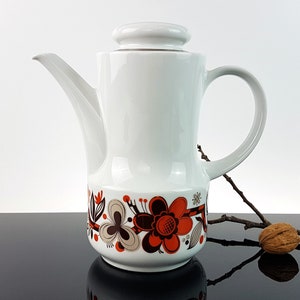 May include: White ceramic coffee pot with a floral design in shades of orange, brown, and white. The pot has a lid and a handle.