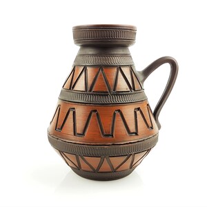 Könnte beinhalten: Eine braune Keramikvase mit geometrischem Muster. Die Vase hat einen breiten Boden und einen schmalen Hals mit einem Henkel.
