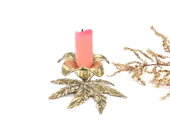 Puede incluir: Un candelero de metal dorado con un diseño de hojas y una vela rosa. El candelero tiene forma de flor con cinco pétalos.