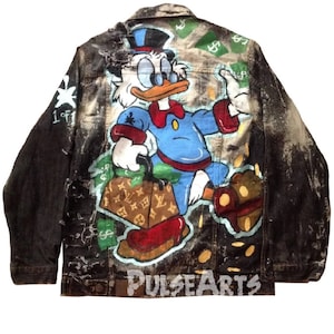 May include: A black denim jacket with a distressed look, featuring a hand-painted design of a cartoon duck character holding a Louis Vuitton bag and surrounded by dollar bills. The jacket has a 'PULSEARTS' logo on the bottom.
