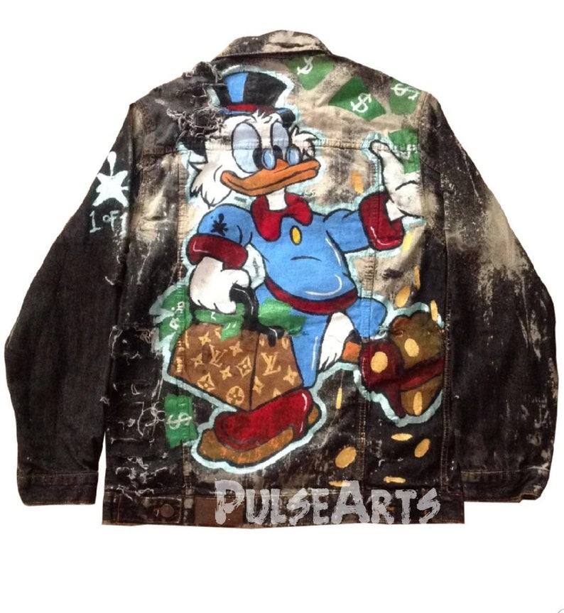May include: A black denim jacket with a distressed look, featuring a hand-painted design of a cartoon duck character holding a Louis Vuitton bag and surrounded by dollar bills. The jacket has a 'PULSEARTS' logo on the bottom.