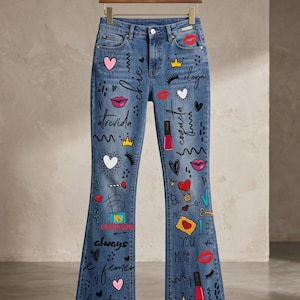 Peut inclure: Jean flare en denim bleu orné de divers motifs graphiques colorés, notamment des cœurs, des couronnes, des lèvres, des flacons de vernis à ongles et des textes manuscrits comme chic, atrevida, coqueta, My valentine, always et YOU Miss.