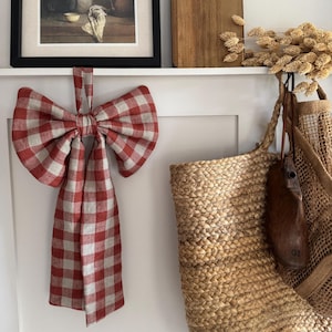 May include: A large, decorative bow made of red and white checkered fabric hangs on a white surface. A woven basket and a framed picture are also visible. The bow is the focal point, adding a rustic touch to the setting.