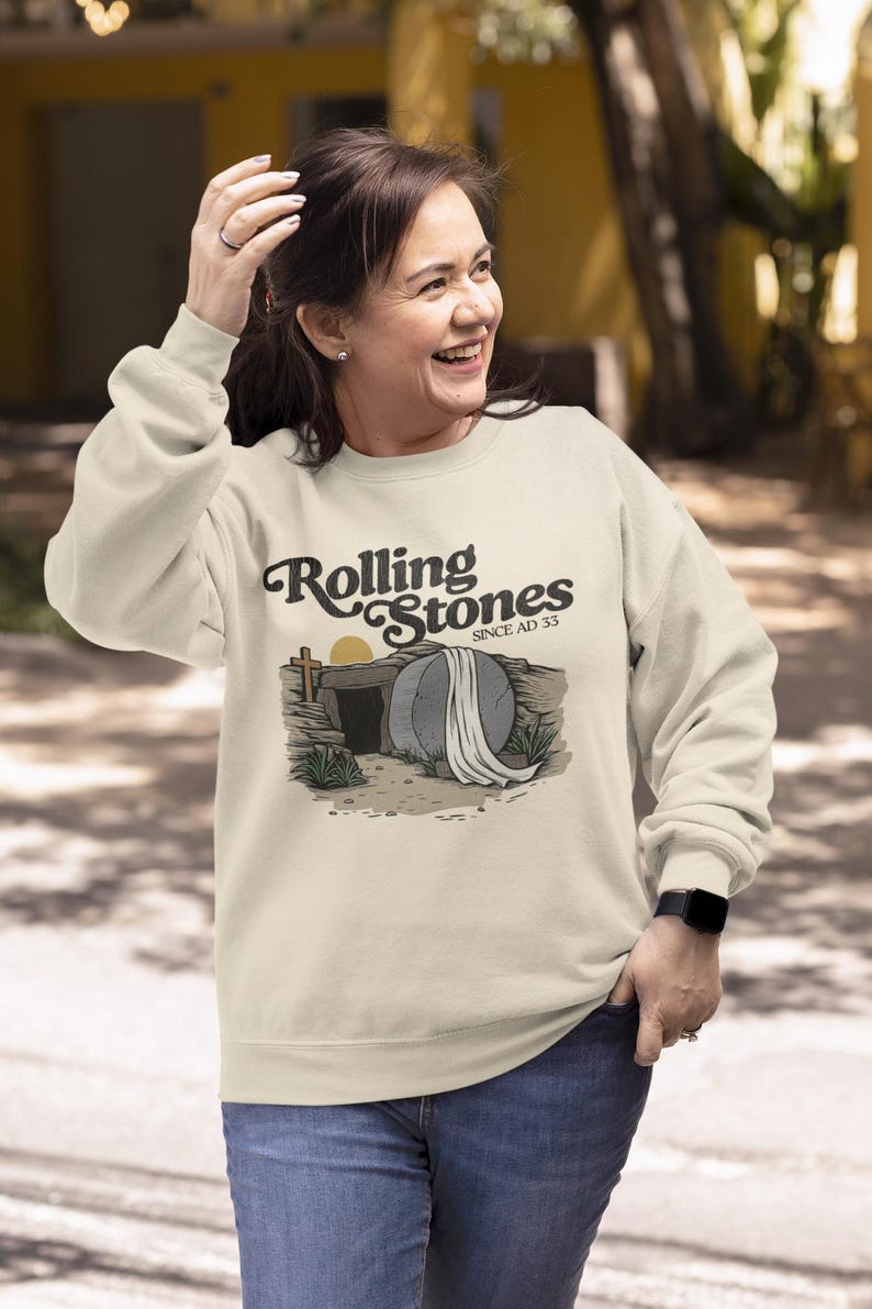 May include: Cream-colored sweatshirt with the text "Rolling Stones Since AD 33" above an illustration of a tomb with a cross and a rising sun. The sweatshirt is long-sleeved and has a crew neck.