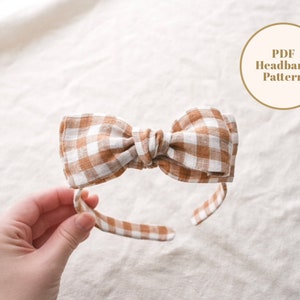 May include: A brown and white gingham headband with a bow. The headband is made of fabric and is tied in a bow at the top. The headband is on a white background. PDF Headband Pattern.