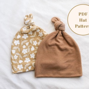 Puede incluir: Dos gorros de punto, uno con estampado floral y otro marr&oacute;n liso. Ambos gorros tienen un nudo en la parte superior. El texto "PDF Hat Pattern" es visible en la imagen.