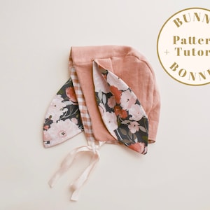 Può includere: Un berretto da coniglio rosa e floreale con un nastro bianco. Il berretto ha un motivo di fiori rosa e bianchi su sfondo scuro. Il testo "Bunny Pattern + Tutorial Bonnet" è in un cerchio dorato.