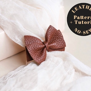 Puede incluir: Un lazo de cuero marrón con un patrón y un tutorial sin coser. El lazo está sobre un fondo de tela blanca. El texto "Leather Pattern + Tutorial No-Sew" está en un círculo negro.