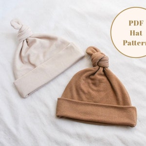 Puede incluir: Dos gorros de punto con un nudo en la parte superior. Un gorro es beige y el otro es marr&oacute;n. El texto "PDF Hat Pattern" est&aacute; en un c&iacute;rculo blanco.