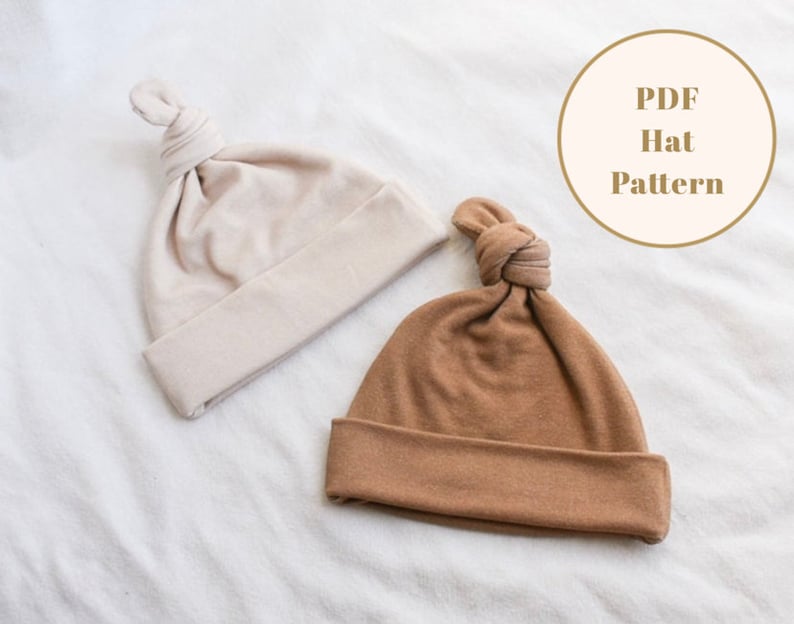 Puede incluir: Dos gorros de punto con un nudo en la parte superior. Un gorro es beige y el otro es marr&oacute;n. El texto "PDF Hat Pattern" est&aacute; en un c&iacute;rculo blanco.