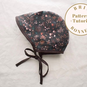 Puede incluir: Un gorro marrón oscuro con estampado floral con flores rosas, blancas y verdes. El gorro tiene una corbata marrón y el texto "BRIM Pattern + Tutorial BONNET" está impreso en un círculo dorado.