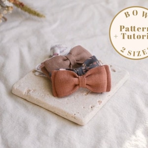 Może przedstawiać: Trzy kokardki z tkaniny w różnych wzorach i kolorach, w tym brązowym, rdzawo-brązowym i czarno-białym. Kokardki są umieszczone na jasnej powierzchni kamiennej. Tekst "BOW Pattern + Tutorial 2 SIZES" jest widoczny w kółku.