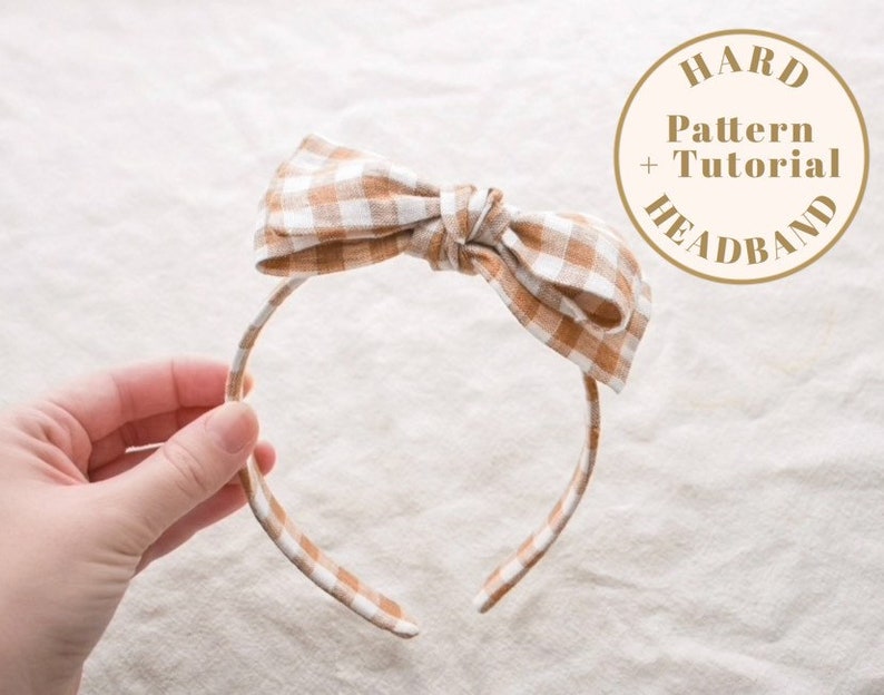 May include: A brown and white gingham headband with a bow. The headband is made of fabric and has a wire frame. The headband is on a white background. The text "HARD PATTERN + TUTORIAL HEADBAND" is on a circle in the upper right corner of the image.