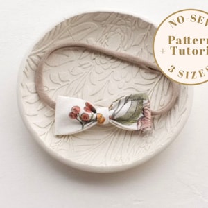 Könnte beinhalten: Ein Stirnband mit Schleife aus Stoff mit Blumenmuster und einem nudefarbenen Gummiband. Das Stirnband wird auf einer weißen Keramik-Schale mit Blumenmuster präsentiert. Der Text "NO-SEW Pattern + Tutorial 3 SIZES" befindet sich auf einem braunen Kreis.