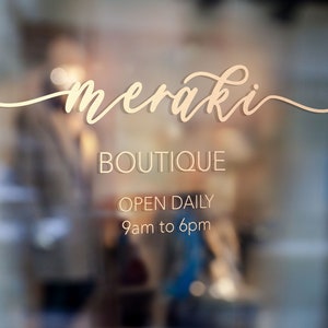 May include: A storefront window with the text "meraki BOUTIQUE OPEN DAILY 9am to 6pm" in gold lettering on a white background.