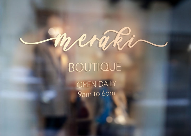 May include: A storefront window with the text "meraki BOUTIQUE OPEN DAILY 9am to 6pm" in gold lettering on a white background.