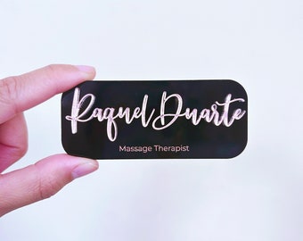 Puede incluir: Tarjeta de visita negra con el nombre "Raquel Duarte" escrito en cursiva rosa y el texto "Massage Therapist" debajo.