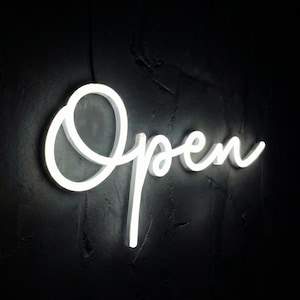 May include: A glowing white neon sign against a dark, textured background. The sign displays the word "Open" in a cursive font, creating a welcoming and illuminated message.
