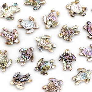 May include: A selection of small, iridescent sea turtle charms. Each charm has a shell with a mosaic-like pattern of colours including pink, purple, and gold. The turtles have a metallic, silver-toned border on a white background.