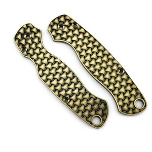 May include: Two brass-colored knife scales with a woven pattern. The scales are curved and have holes for screws. The scales are designed to be attached to a knife handle. The brass color gives the scales a vintage look.